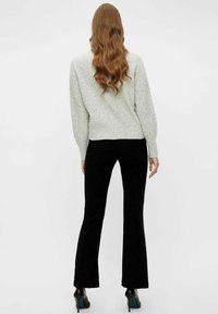 Šedý texturovaný svetr doplněný černými rozšířenými kalhotami. Kalhoty mají přiléhavý pas a rozšířený střih nohavic. Celkový vzhled doplňují černé lodičky.