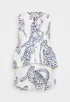 Hvid ærmeløs top med sort og blå leopardprint, der har en flæse i kanten og en knaplukning. Båret sammen med matchende shorts.