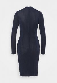 Abito a maniche lunghe, aderente, realizzato in tessuto testurizzato di un blu navy scuro, con scollo alto e zip invisibile sul retro. Taglio al ginocchio.