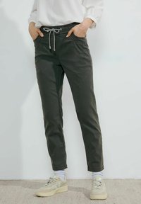 Pantalones ajustados de color verde oscuro con cintura elástica y cordón. Presentan bolsillos laterales y una textura suave similar al algodón.