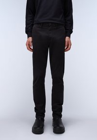 Pantaloni neri in cotone con vestibilità slim, dotati di chiusura con bottone, passanti per cintura e texture liscia, abbinati a scarpe nere.