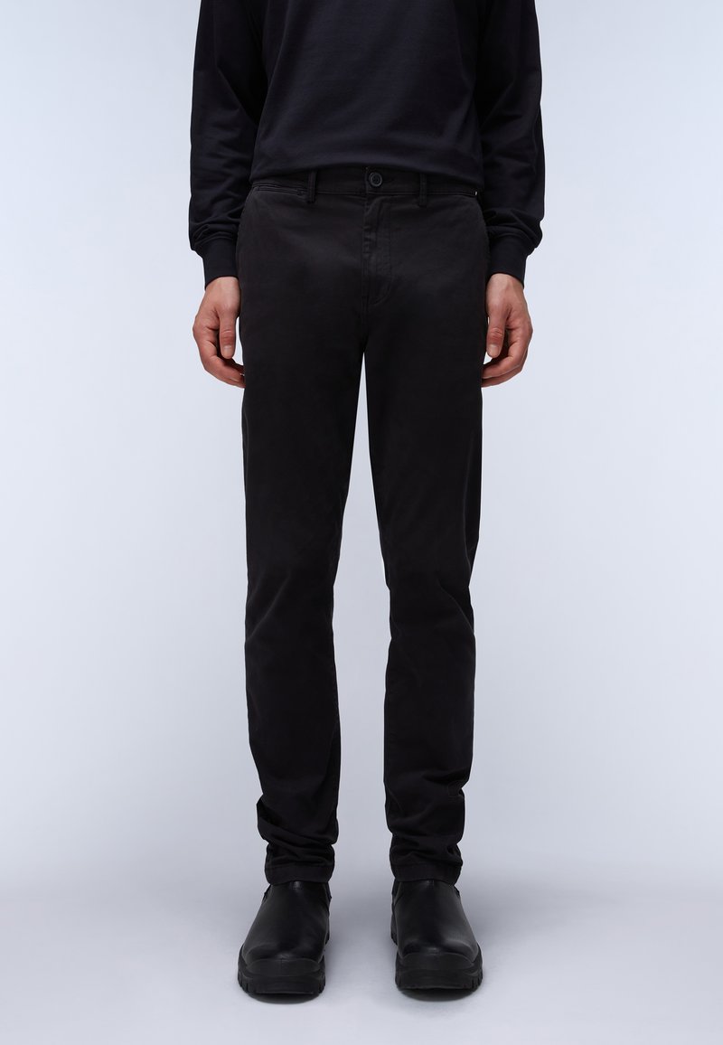 Schwarze Baumwollhosen mit schmaler Passform, mit Knopfverschluss, Gürtelschlaufen und glatter Textur, kombiniert mit schwarzen Schuhen.