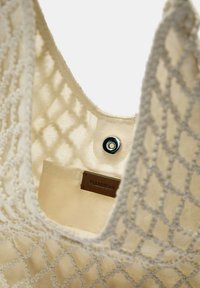 Beige stoffen draagtas met een netachtige buitenkant, voorzien van een metallic drukknoopsluiting en een label binnenin met de tekst "FULLSEAR."