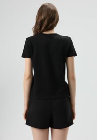 T-shirt noir à manches courtes, en coton doux, avec un col rond classique et une coupe décontractée, associé à un short noir en matériau similaire.