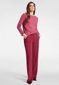 Maglione a maniche lunghe di un leggero rosa con scollatura a girocollo e dettagli con bottoni ai polsini, abbinato a pantaloni larghi bordeaux.