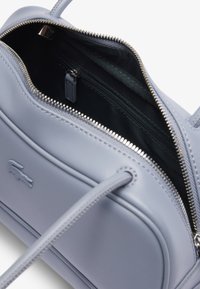 Borsa a mano in pelle grigia chiara con chiusura a zip, tasca interna e accenti testurizzati. Presenta doppi manici per una facile portabilità.