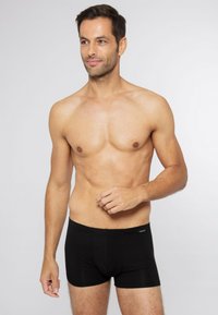 Boxer da uomo neri realizzati in tessuto elasticizzato, caratterizzati da un design aderente con una vita liscia e una texture sottile. Senza ulteriori motivi o dettagli.