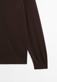 Bruine gebreide mouw van een trui met geribbelde manchetten en onderkant, met een gladde textuur en een licht taps toelopend ontwerp naar de pols.