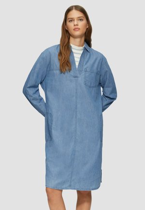 Denim-mekko, jossa on väljä istuvuus, pitkät hihat, V-pääntie, rintatasku ja sivutaskut. Vaaleansininen väri ja sileä pinta.
