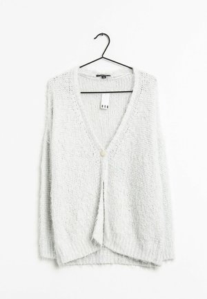 Cardigan en maille blanche duveteuse à manches longues avec un seul bouton sur le devant, suspendu sur un cintre noir sur fond blanc.