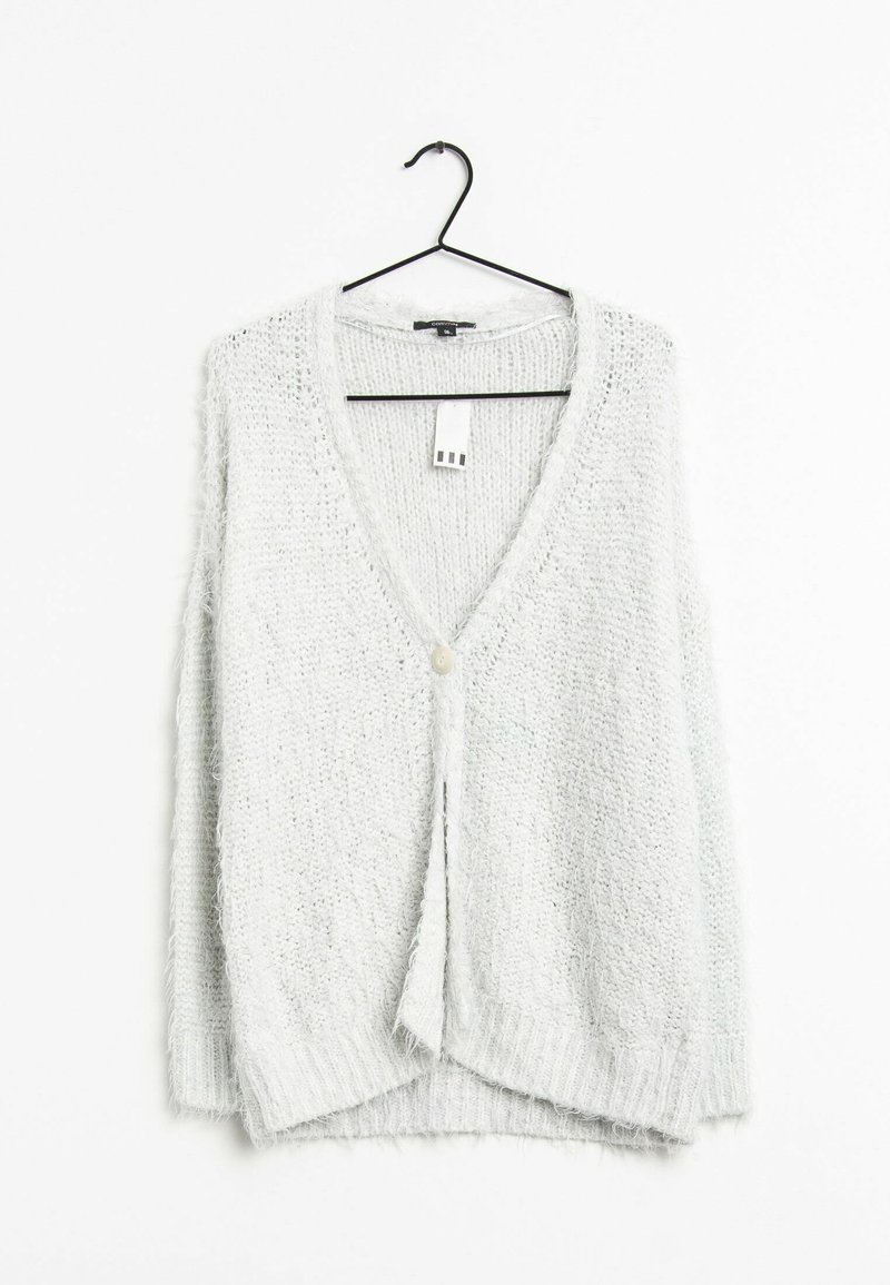 Cardigan en maille blanche duveteuse à manches longues avec un seul bouton sur le devant, suspendu sur un cintre noir sur fond blanc.