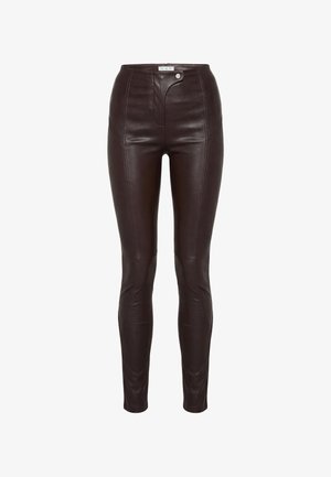 Ciemnobrązowe spodnie ze skóry z wysokim stanem, z przeszyciami z przodu oraz asymetrycznym zapięciem na guziki i zatrzaski w pasie.