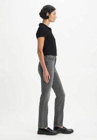 Black textured short-sleeve top with a collar paired with high-waisted gray jeans and black platform shoes, displayed from the side.