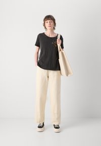 Maglietta grigia scura a maniche corte con grafica del sole, abbinata a pantaloni a gamba larga di colore crema e sneakers nere con suola bianca.