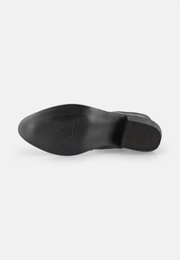 Suela de zapato negra, diseño plano, fabricada con material similar a la goma, cuenta con agarre texturizado, nombre de marca en relieve y líneas limpias sin patrones.