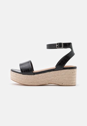 Sorte platform sandaler i krokodillemønster med bred forreste rem, ankelrem med spænde og vævet jute mellemsål, der har en afrundet tå.