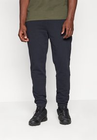 Marineblauwe sweatpants met een tapered fit, elastische manchet, en zijzakken, gecombineerd met zwarte sportschoenen met textuur en veters.