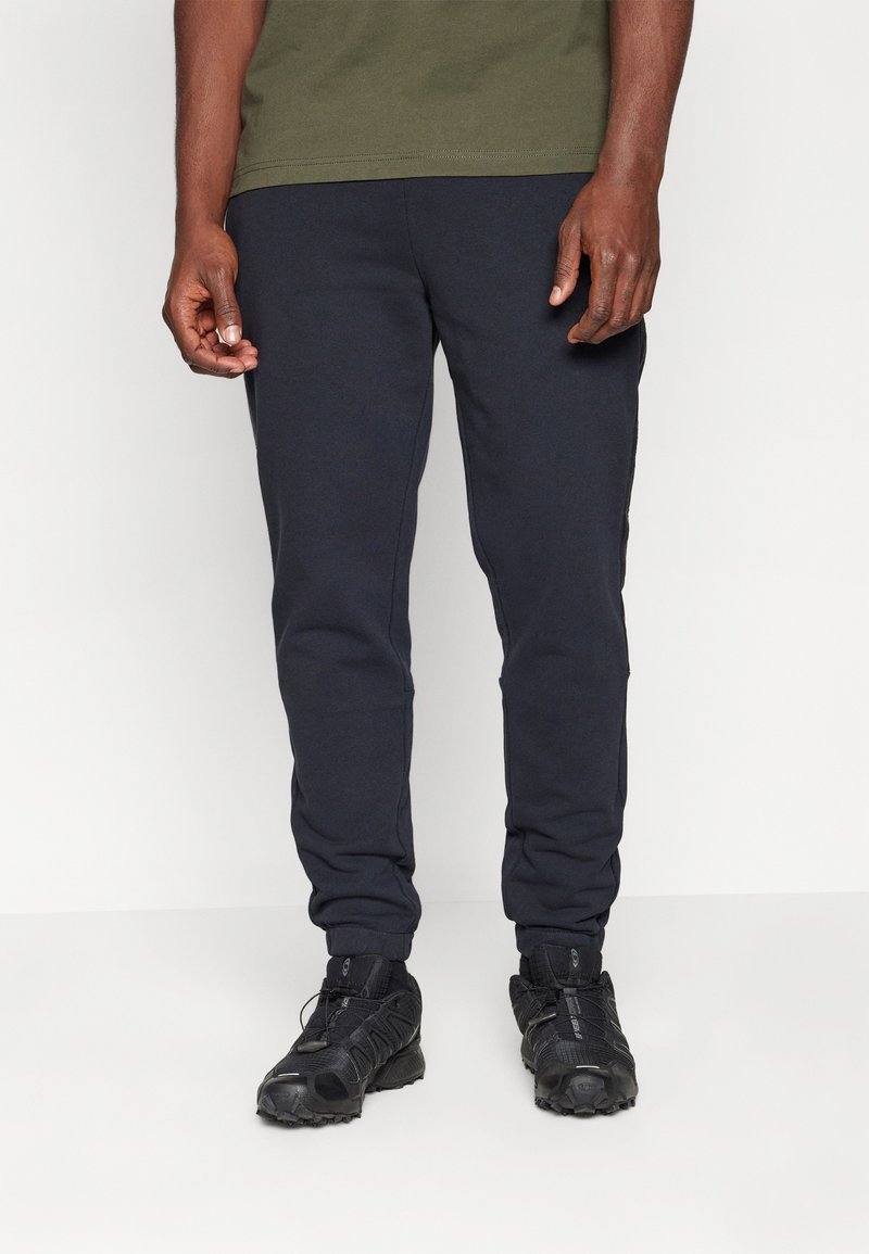 Marineblauwe sweatpants met een tapered fit, elastische manchet, en zijzakken, gecombineerd met zwarte sportschoenen met textuur en veters.