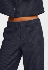 Marina herringbone-mönstrade byxor med en jämn textur, med midjeband och framfickor, kompletterade av subtila sömdetaljer.