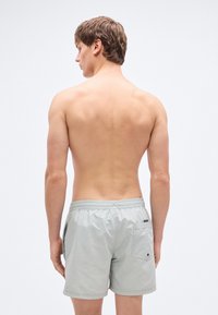 Ανοιχτό γκρι μαγιό σορτς με ελαστική μέση, μια πίσω τσέπη και λεία υφή υφάσματος. Προβολή από πίσω, το μοντέλο δεν φοράει μπλούζα.