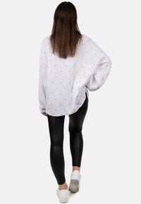 Witte lange mouwen top met roze hartpatronen, gecombineerd met zwarte leggings en witte sneakers. Losse pasvorm met wijde mouwen en een gebogen zoom.