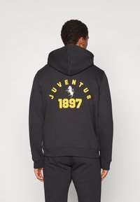 Svart hoodie i bomull med en stor gul "JUVENTUS" och en vit hästlogotyp med "1897" på baksidan. Mjuk textur, normal passform.