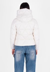 Witte pufferjack met een gequilt geometrisch patroon, een capuchon en een cropped pasvorm, gecombineerd met losse blauwe spijkerbroek.