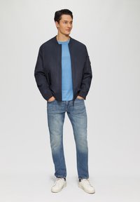 Marynarka bombowa w stylu marynarskim, niebieska koszulka, jasnoniebieskie dżinsy i białe trampki. Gładki materiał, zapięcie na zamek, elastyczne mankiety i przednie kieszenie.