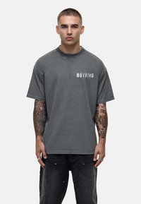 Grijze katoenen T-shirt met korte mouwen, voorzien van een gedurfde "NOTHING" grafische print in het wit. Het ontwerp is oversized en heeft een relaxte pasvorm.
