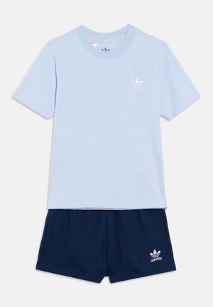 Camiseta de manga corta y cuello redondo de Adidas en azul claro combinada con pantalones cortos de Adidas en azul marino, ambos con el logo de trébol blanco de Adidas.