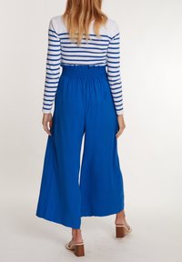 Pantalons larges bleus avec une taille élastique associés à un haut à rayures à manches longues. Tissu lisse avec une coupe décontractée.