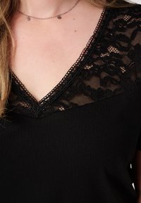 Zwarte top met een V-hals en ingewikkelde zwarte kantdetails en ribbeltextuur. Korte mouwen en delicate kantafwerking langs de halslijn.