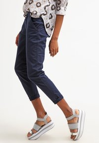 Marina blå capribyxor med sidofickor, tillsammans med grå sandaler med en texturerad rem och en chunky vit plattformssula.