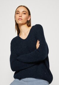 Marineblauwe, oversized trui met een brede halslijn en lange mouwen. Gemaakt van een zachte, gestructureerde stof; voorzien van een klein logo detail aan de zoom.