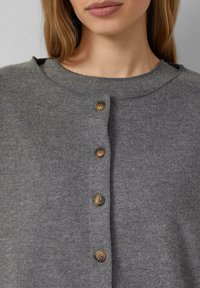 Grauer Strickcardigan mit rundem Halsausschnitt und fünf braunen Knöpfen auf der Vorderseite. Weiche Textur und gerippte Stoffdetails.