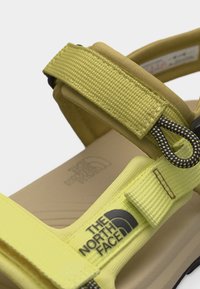 Κίτρινο σανδάλι με ρυθμιζόμενο λουράκι, λεπτομέρεια σε μαύρο και λευκό βρόχο και το λογότυπο της The North Face στο λουράκι και στη σόλα.