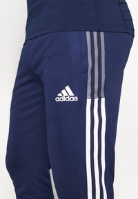 Marineblauwe sportbroek met een wit drie-strepen ontwerp, gemaakt van ademend materiaal. Bevat een geborduurd wit Adidas-logo op de dij.