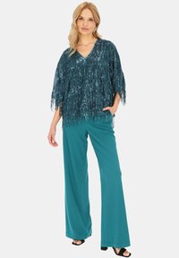 Turkusowy top z frędzlami i cekinami, dekolt w serek, w połączeniu z szerokimi turkusowymi spodniami i czarnymi szpilkami. Gładka tekstura i luźny krój.