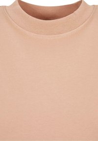 Gros plan du col rond d'un t-shirt beige montrant la texture en maille côtelée et le tissu lisse sous l'encolure.