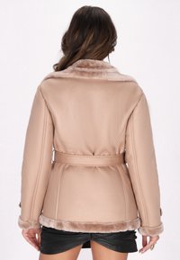 Beige nepleer jacket met een zachte bontkraag, tailleband en luxe mouwen. Heeft een gestructureerd oppervlak en afgeronde randen.