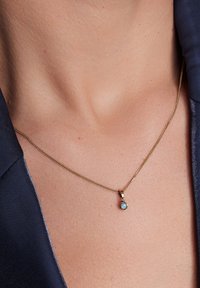 Złoty naszyjnik z skręconym łańcuchem i małym niebieskim kamieniem wisiorkiem, spoczywający na skórze i ustawiony na granatowym tle z tkaniny.