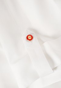 Poignet de chemise blanc avec un bouton rouge présentant un motif de pomme tranchée cousu sur le tissu.