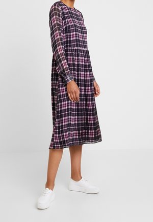 Langemouwen geruite jurk met een zwart, paars en roze ruitpatroon, uitlopende rok en zakken, gecombineerd met witte sneakers.