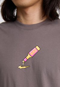 Grå t-shirt med et farverigt grafik af en dryppende flaske mærket "NIKE" i pink og gul, med en glat tekstur.