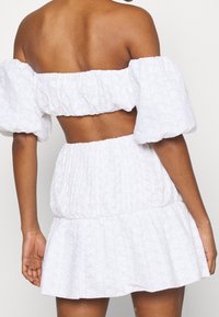 Vestido blanco sin hombros con mangas abullonadas, cuerpo fruncido y falda en capas. Textura con patrón floral en toda su extensión. Acabado de tela suave.