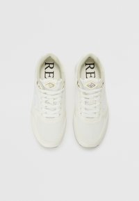 Zapatillas deportivas blancas con parte superior de malla, diseño con cordones y acentos dorados. Presenta un cuello acolchado y suela de goma texturizada.