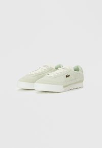 Pareja de zapatillas de ante verde claro con cordones blancos, suelas de goma y un pequeño logo de cocodrilo en el costado.