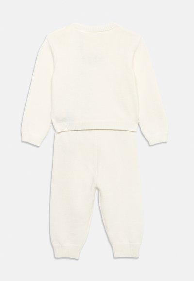 Ensemble pour bébé composé d'un haut à manches longues en tricot blanc et d'un pantalon assorti, avec poignets et taille côtelés, présenté de dos sur un fond uni.