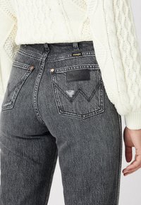 Vaqueros de mezclilla negros de cintura alta con un lavado desvanecido, que cuentan con una etiqueta de cuero, remaches de cobre y dos bolsillos traseros con detalles de costura.