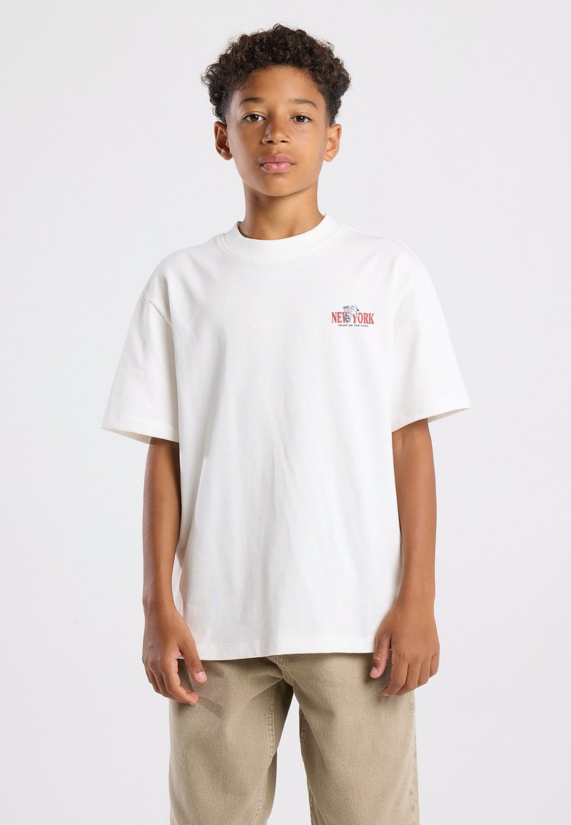Valkoinen puuvilla t-paita lyhyillä hihoilla, pyöreällä kaula-aukoksi, jossa on pieni punainen "NEW YORK" -grafiikka vasemmassa rintakehässä.